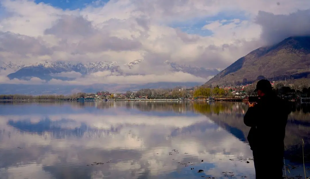 A man takes photograph of snow-clad mountains reflected in Dal Lake after rains, in Srinagar | Photo: PTI