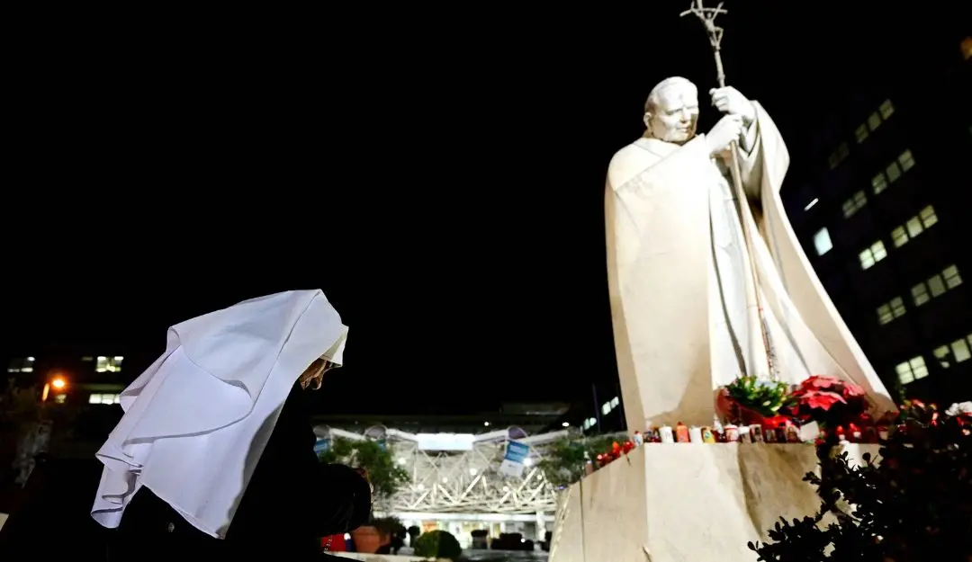 A nun prays in front of a statue of Pope John Paul II outside the Gemelli hospital where Pope Francis is hospitalized for tests and treatment for bronchitis in Rome | Photo: AFP