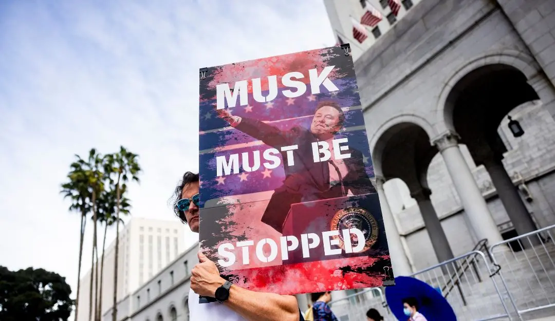 A demonstrator holds a poster of Elon Musk during a rally to protest President Trump's policies | Photo: AP