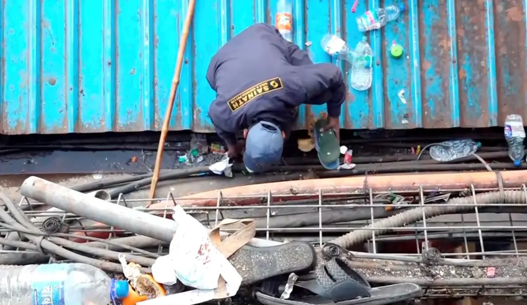 A cleaning staff collects belongings of passengers scattered on a tin shed a day after a stampede