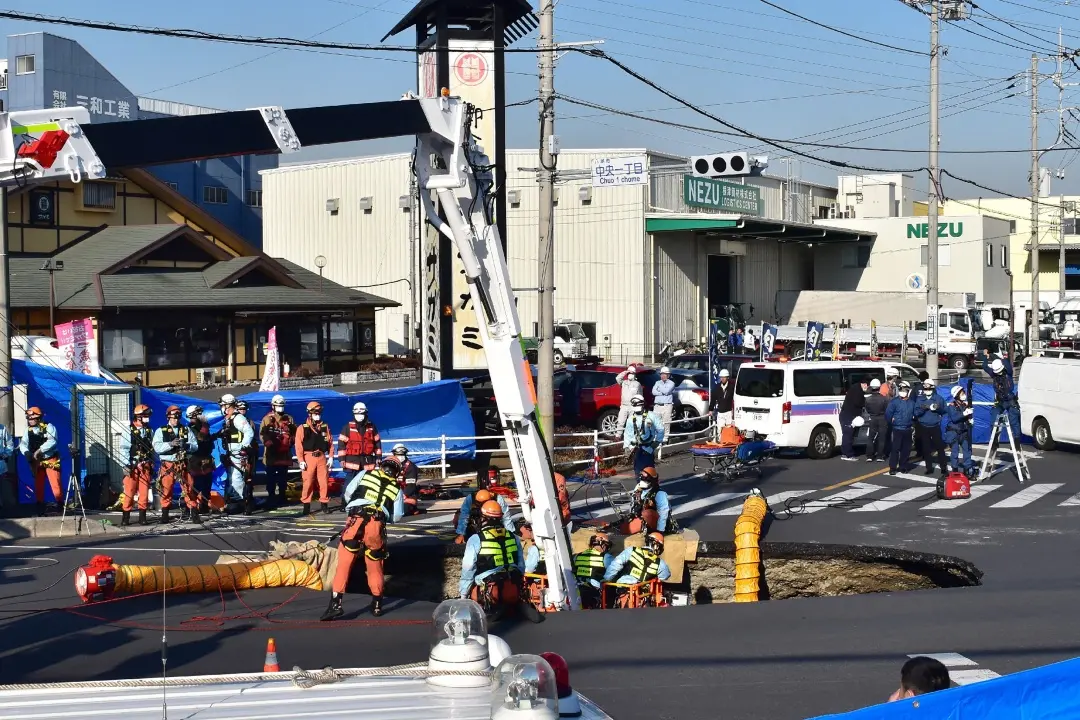Firefighters work to rescue a truck driver after his vehicle was swallowed up by a sinkhole at a prefectural road intersection, in the city of Yashio | Photo: AFP