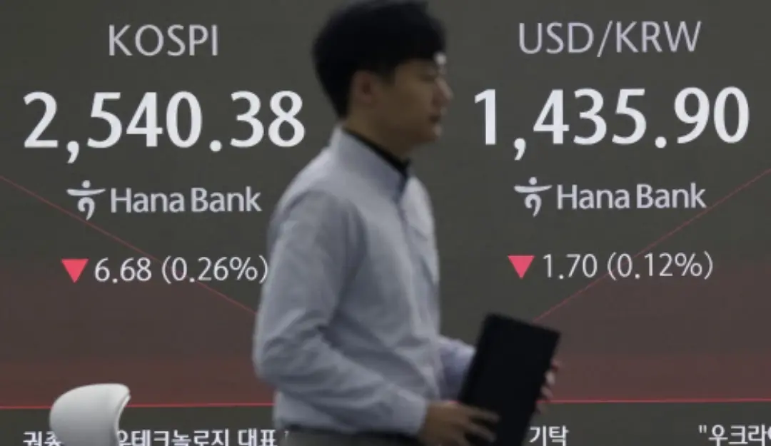 A currency trader passes by a screen showing the Korea Composite Stock Price Index (KOSPI), left, and the foreign exchange rate between U.S. dollar and South Korean won at the foreign exchange dealing room of the KEB Hana Bank headquarters in Seoul, South Korea, Thursday, Jan. 23, 2025.