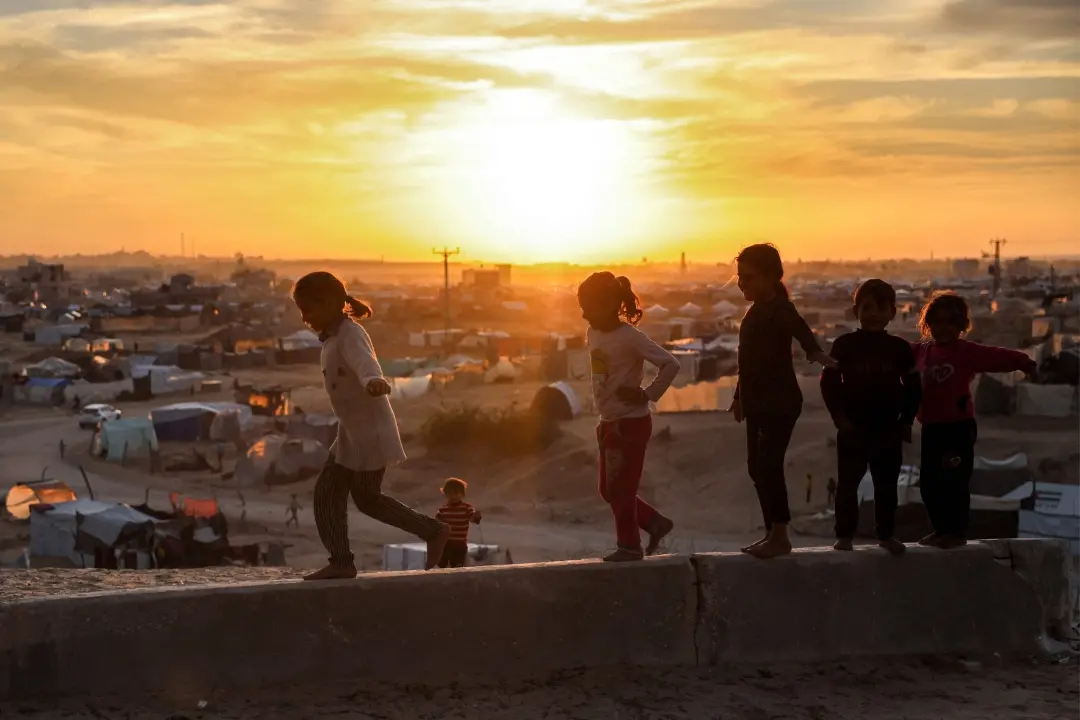 Children walk on a ledge near tents sheltering Palestinians displaced by conflict, Gaza | Photo: AFP
