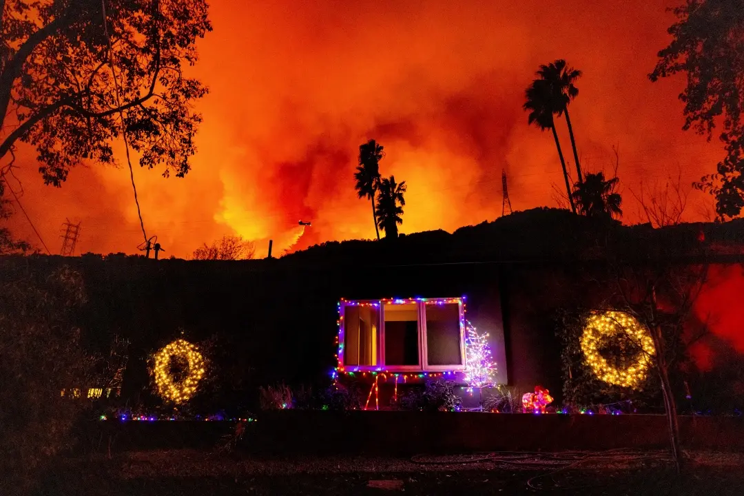 A helicopter drops water on the Palisades Fire behind a home with Christmas lights in Mandeville Canyon | Photo: AP