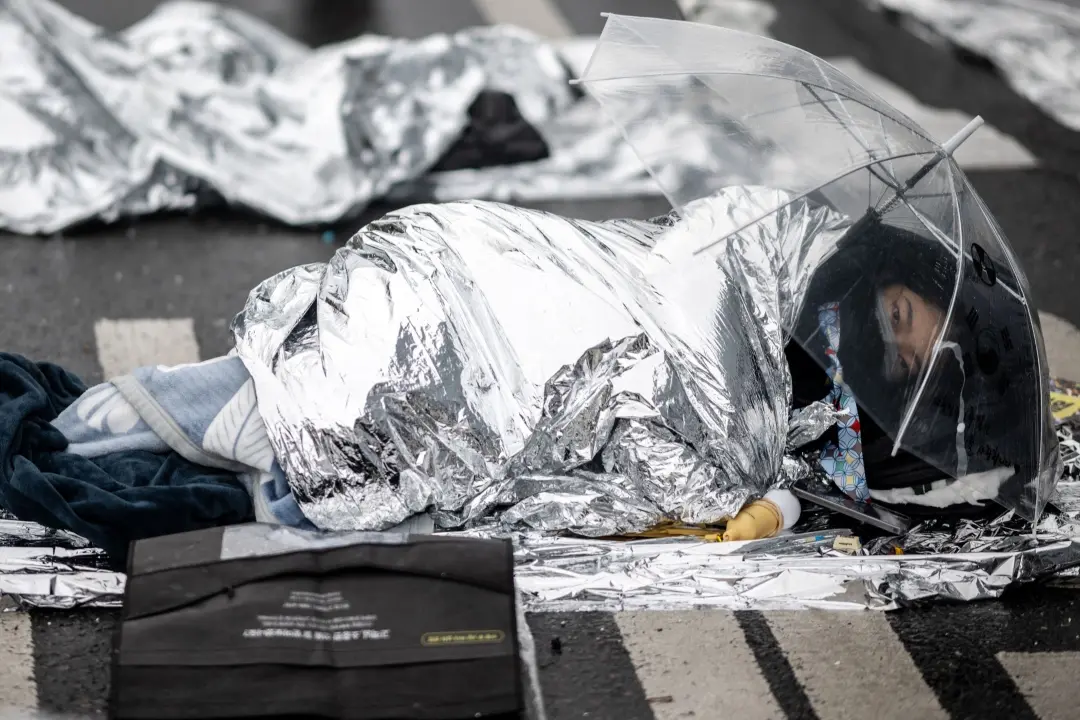 A demonstrator using thermal blankets rests during a rally against impeached South Korean President Yoon Suk Yeol near his residence in Seoul on Monday | Photo: AFP