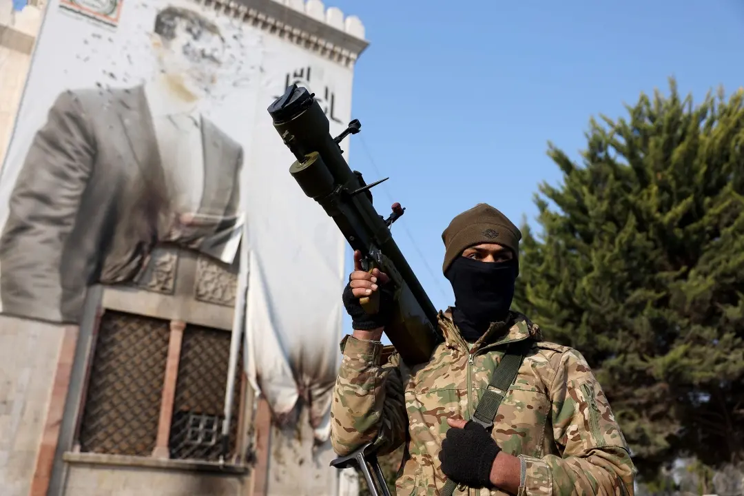 Opposition fighter holds a weapon as he keeps position near a defaced portrait of Syrian President Bashar al-Assad | Photo: AFP