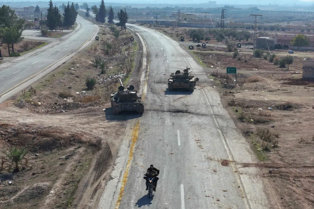 An aerial picture shows anti-government figthers riding a motorcycle past Syrian army military equipment and vehicles that were abandoned on the highway to Damascus | AFP