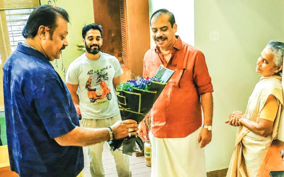 Suresh Gopi speaking about the violet flower bouquet he brought while paying a visit to Sathyan Anthikad's home as the director's wife Nimmy and son Anoop Sathyan look on