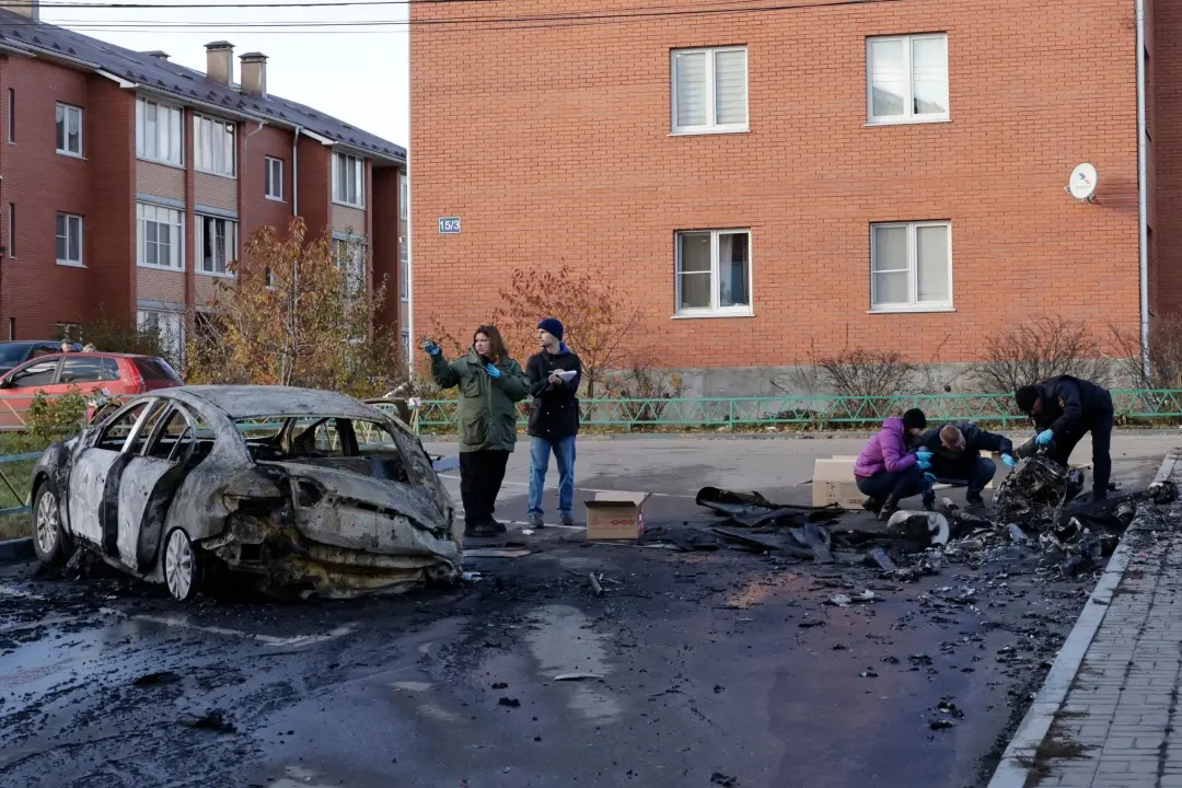 Russian law enforcement officers inspect the wreckage of a drone next to a burnt-out car