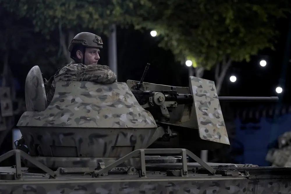 A Lebanese army soldier sits behind his weapon on the top of an armored personnel carrier at the site of an Israeli airstrike in Beirut's southern suburb | AP