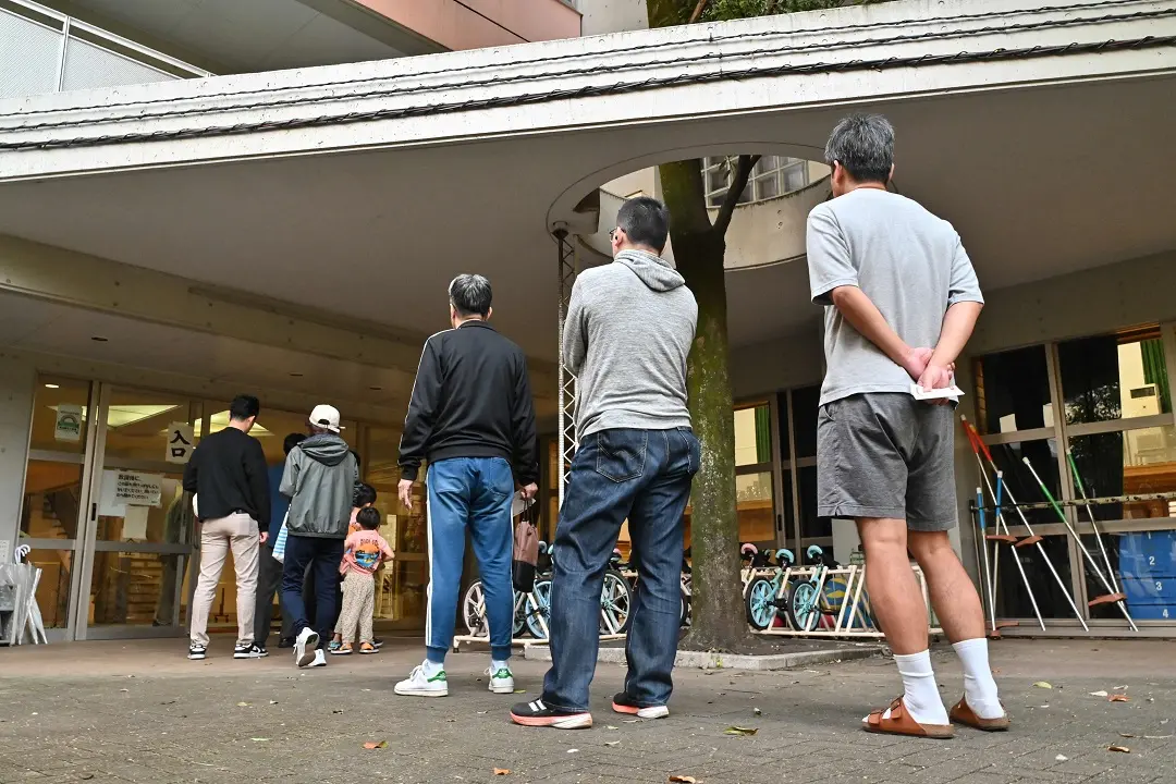 People queue up outside a polling station set up at a local school to cast their ballot in the general election in Tokyo | Photo: AFP