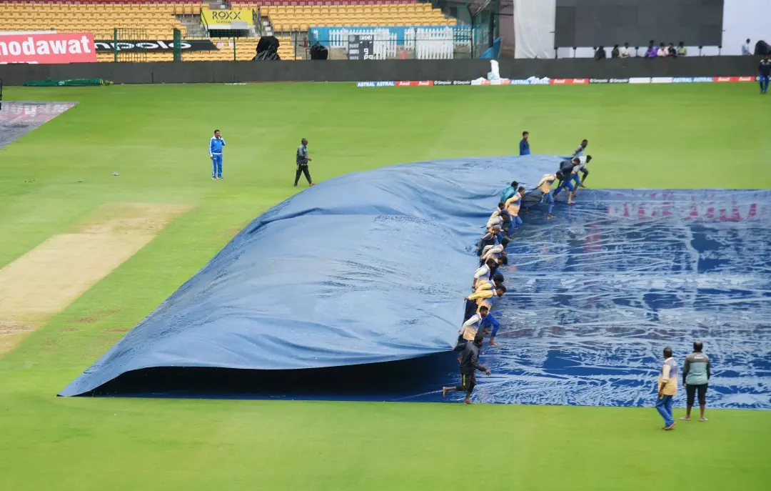 Groundmen cover pitch as it drizzles ahead of the first Test cricket match between India and New Zealand at the M Chinnaswamy Stadium in Bengaluru on Tuesday. | Photo: IANS