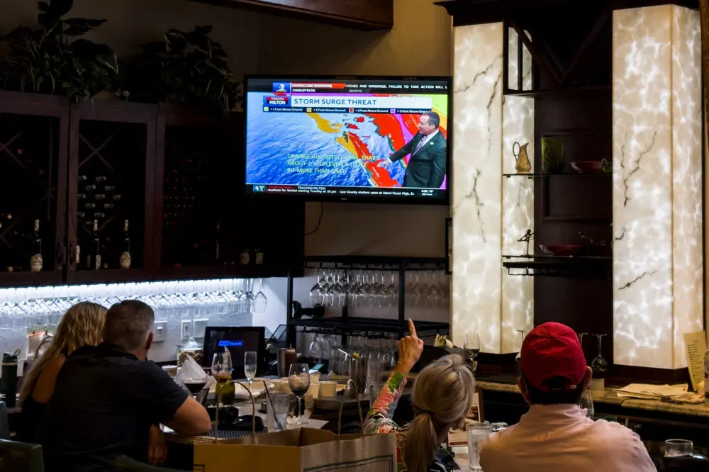 A woman points to the television as people watch the weather report in a restaurant in Fort Myers, Florida | AFP