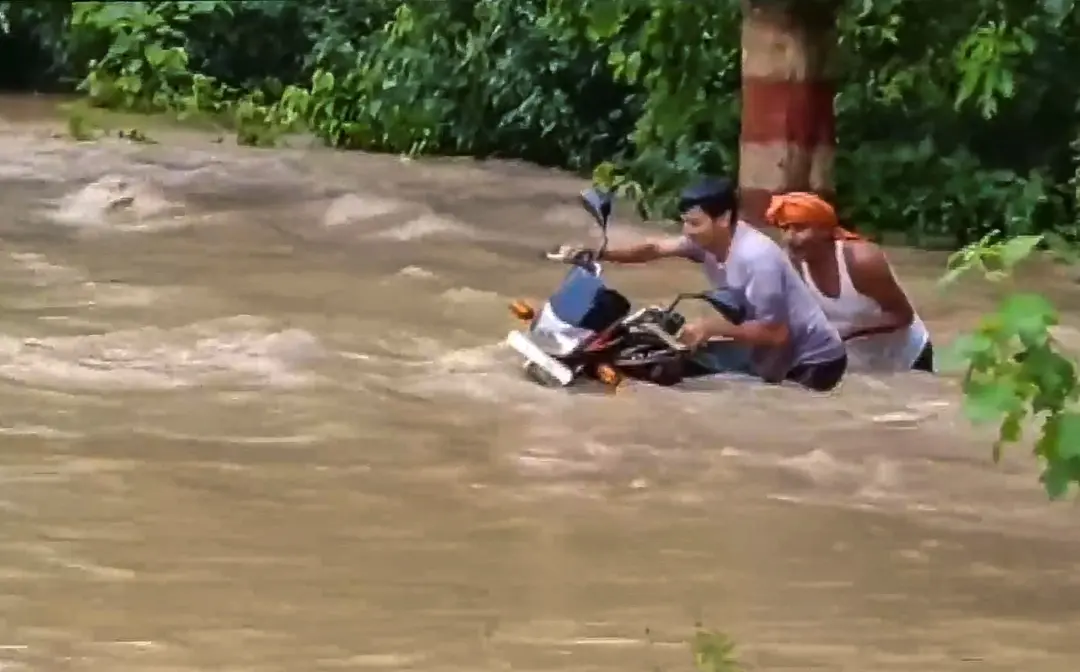Commuters wade through a flooded area after an increase in the water level of Gandak river due to heavy rainfall, in Bagaha, Bihar