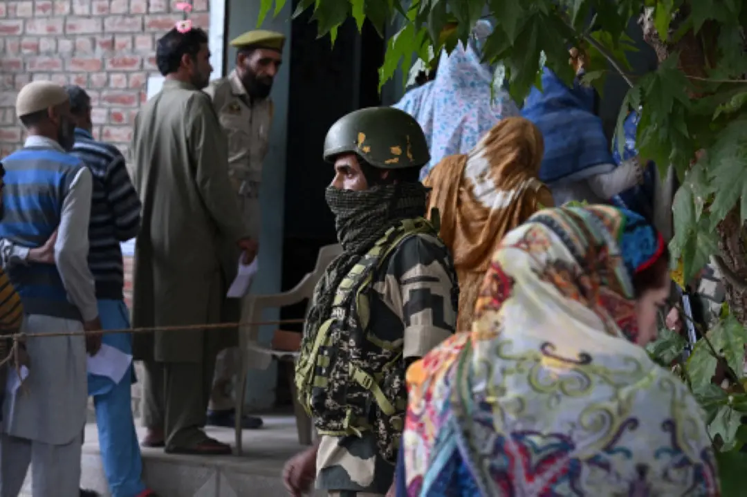 An Indian security personnel stands guard as voters queue up to cast their ballots at a polling station during the first phase of assembly elections in Pulwama, south of Srinagar on Wednesday. | Photo: AFP