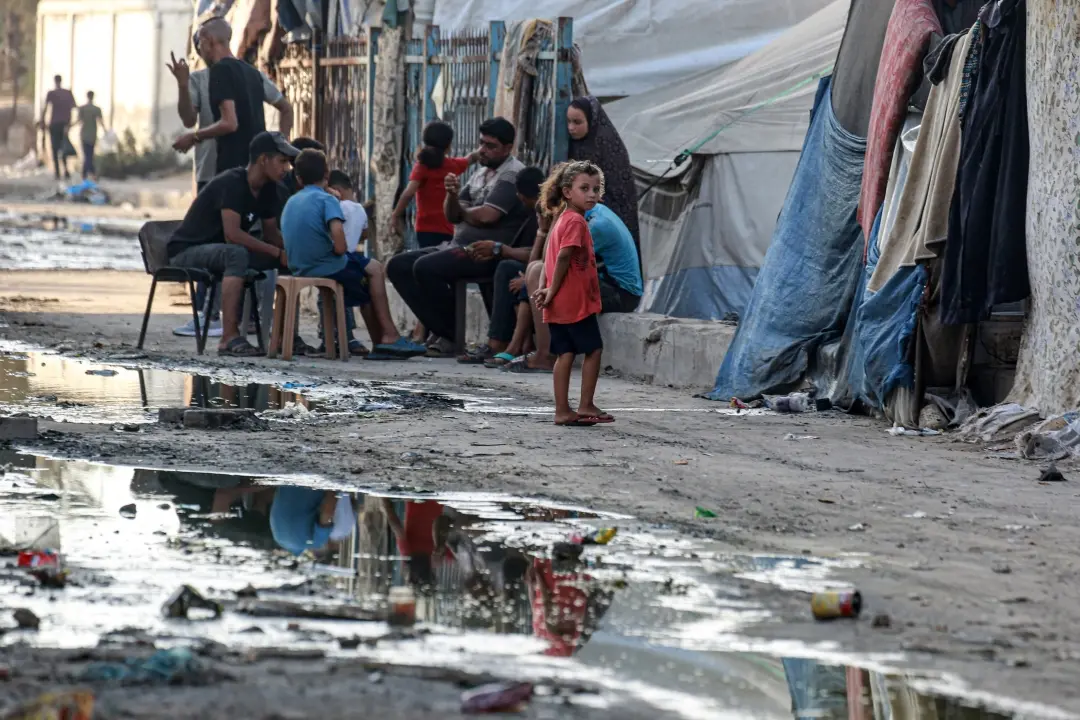 Palestinians walks near tents used as shelter along a street covered with stagnant wastewater in Deir el-Balah in the central Gaza Strip