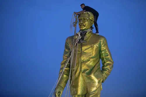 A man climbs to tie a rope around the head of a large statue of Sheikh Mujibur Rahman, father of Bangladesh leader Sheikh Hasina, as protesters try to bring it down after she resigned as Prime Minister, in Dhaka, Bangladesh. | Photo: AP