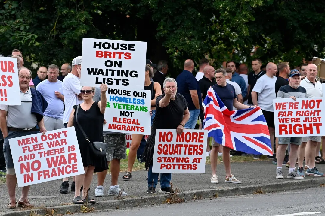 Protesters hold placards during a 'Enough is Enough' demonstration called by far-right activists in Aldershot | Photo: AFP