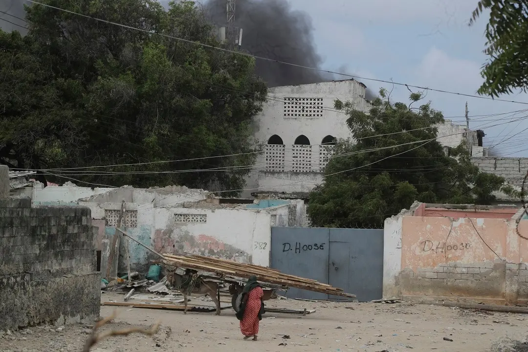 A woman walks on the beach as black smoke is seen rising in the background following an attack in Mogadishu, Somalia | Photo: AP