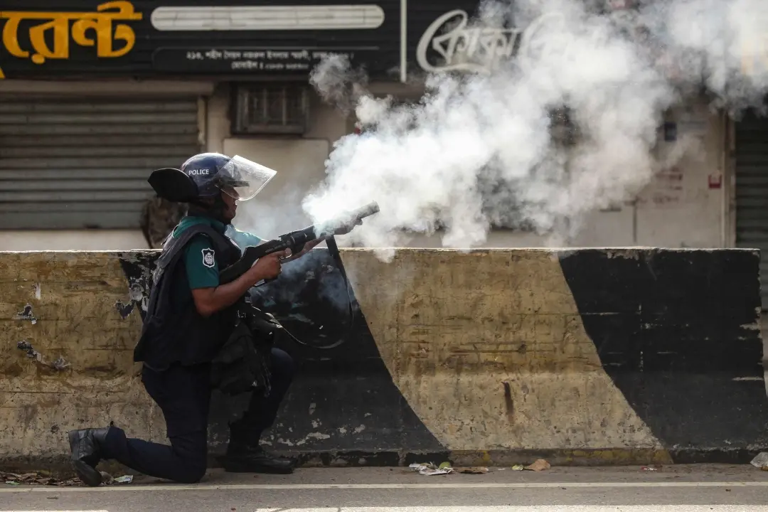 A Bangladeshi policeman fires tear shells to disperse anti-quota protesters during a clash in Dhaka