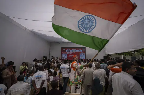A Congress party supporter waves an Indian flag as others follow proceedings of vote counting on a giant screen at their party headquarters in New Delhi. l Photo: AFP
