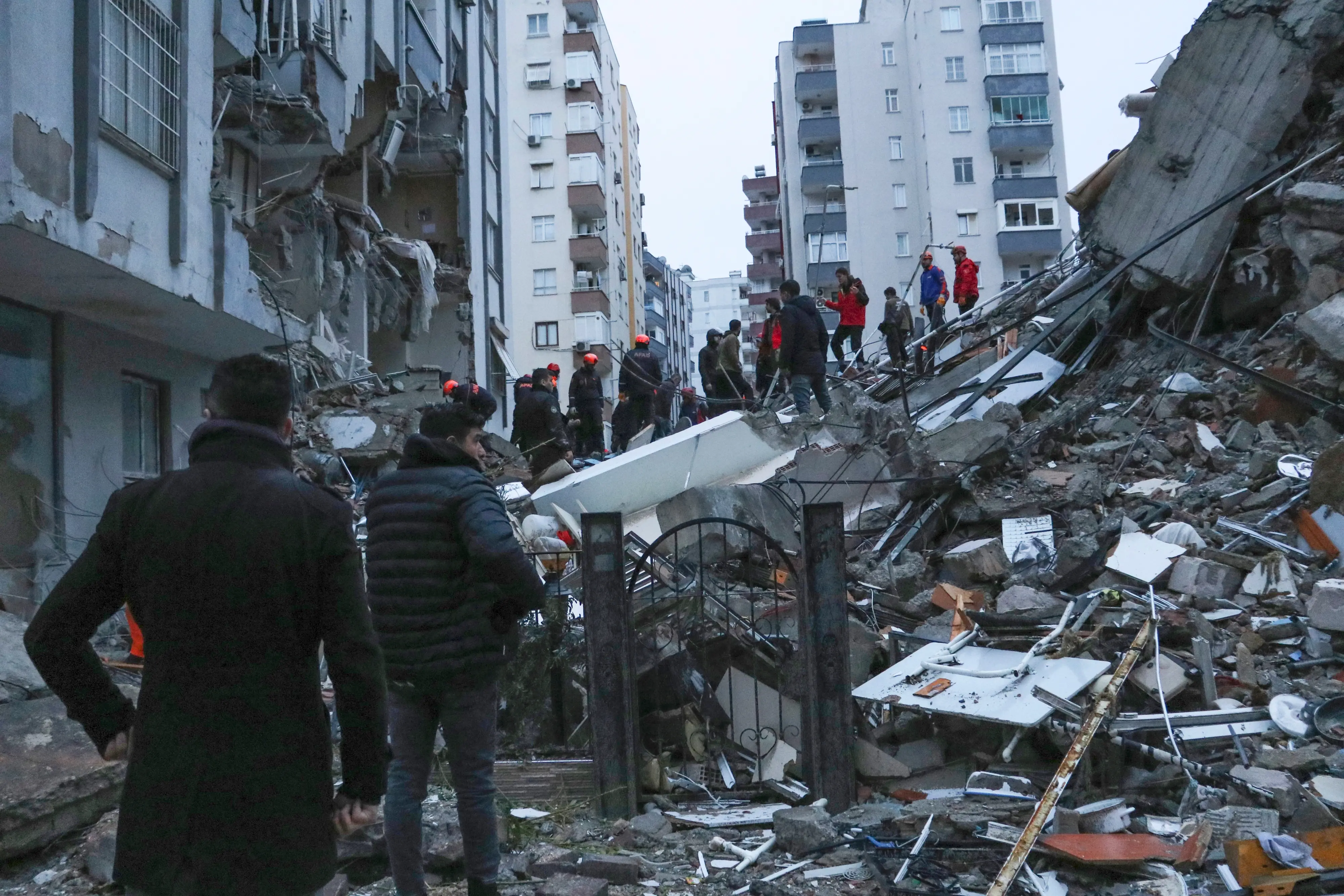People and rescue teams try to reach trapped residents inside collapsed buildings in Adana, Turkey | Photo: AP