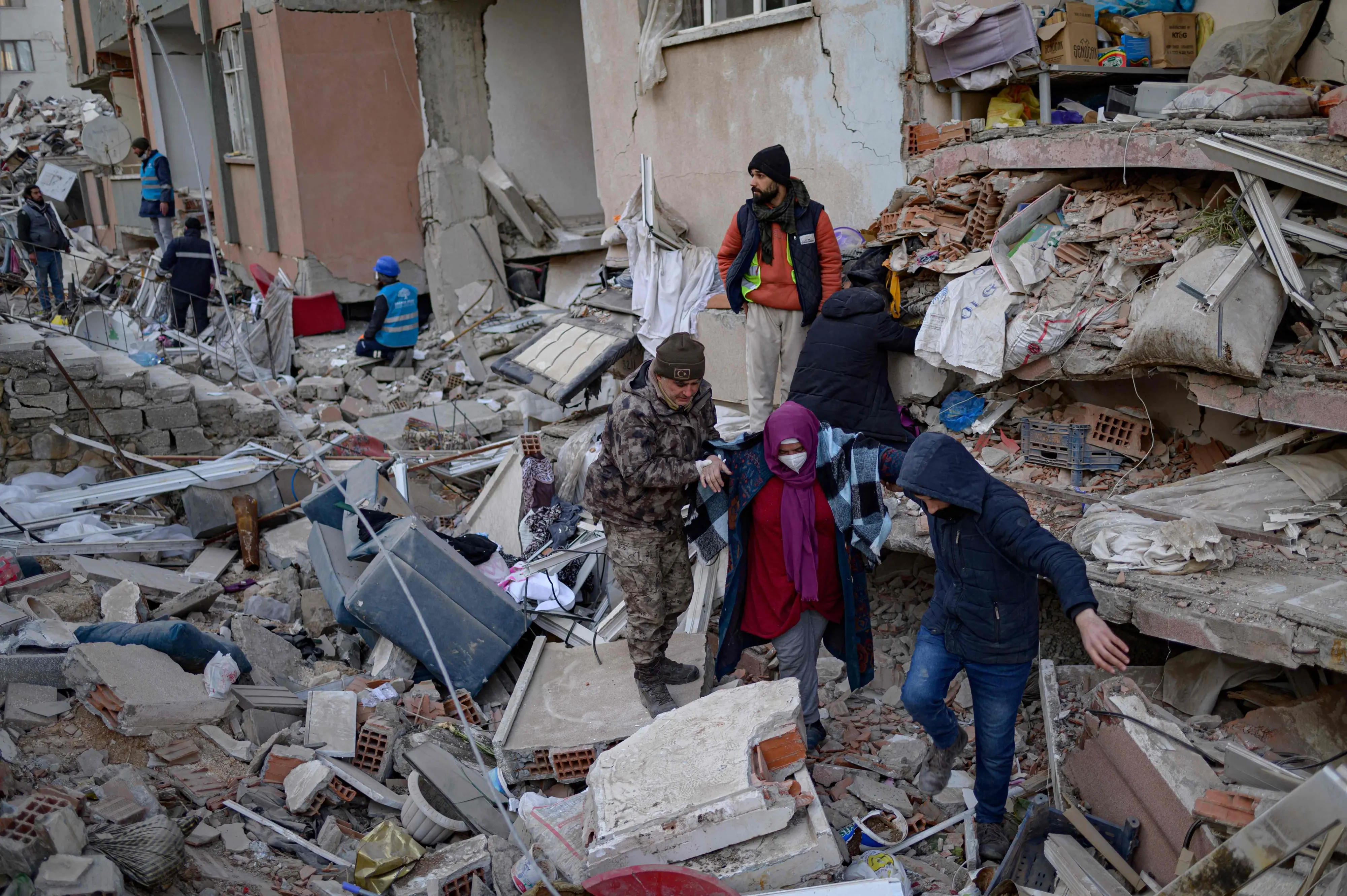 A woman looking for her relatives in the rubble of collapsed buildings is escorted, in Hatay | Photo: AFP