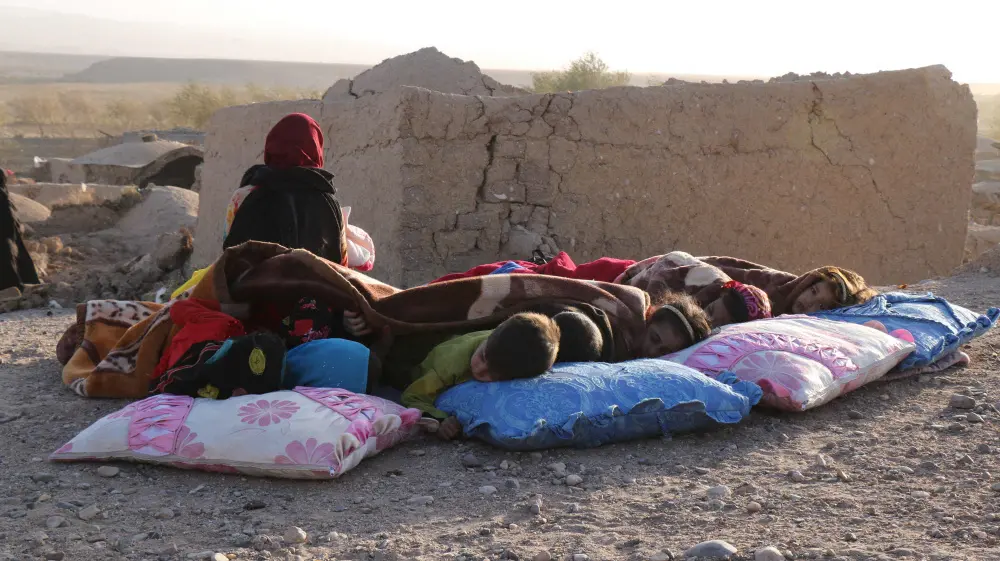 Afghan children rest under a blanket beside damaged houses after earthquake | AFP