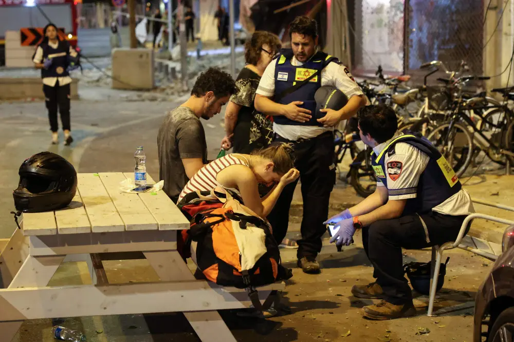 A young woman reacts as she speaks to Israeli rescuers in Tel Aviv, after a was hit by a rocket fired by Palestinian militants from the Gaza Strip | AFP