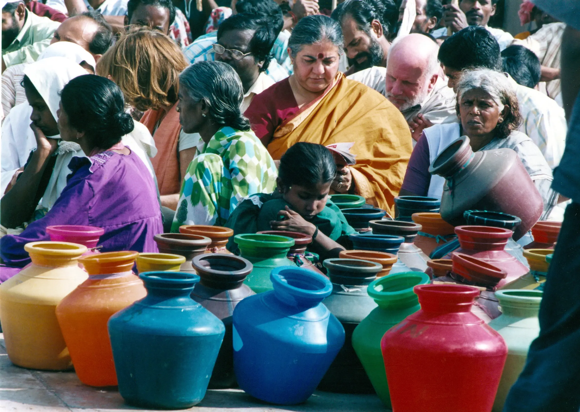 A group of people sit around some vases. Myilamma {right foreground} has an intense look, even as Dr Vandana Shiva is immersed in reading and behind her, the Canadian Tony Clarke of Polaris Institute intently listens to a delegate | photo: C R Girish Kumar