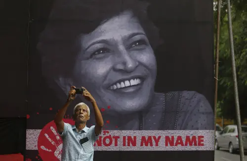 A man takes a photographs during a protest condemning the killing of journalist Gauri Lankesh, protrait in background | AP photo