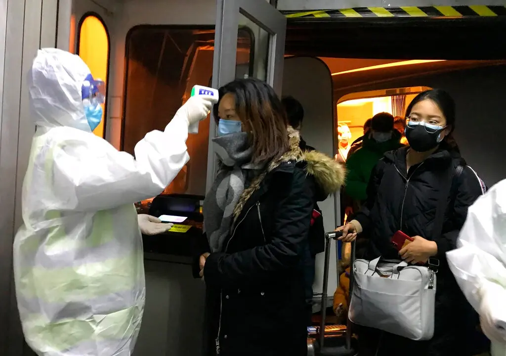 Health Officials in hazmat suits check body temperatures of passengers arriving from the city of Wuhan at the airport in Beijing