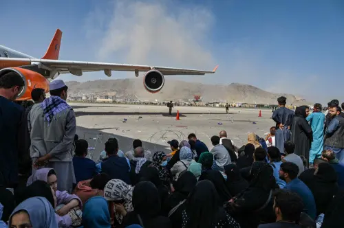 Afghan people sit as they wait to leave the Kabul airport I Photo: AFP
