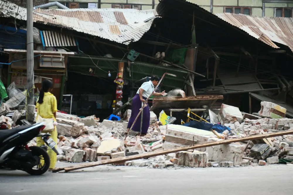 A woman clears debris in front of damaged houses in Mandalay, two days after an earthquake struck central Myanmar | AFP