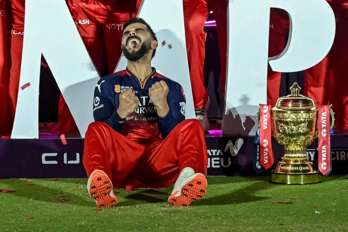 Royal Challengers Bengaluru's Virat Kohli reacts while sitting beside the trophy after winning the Indian Premier League (IPL) Twenty20 final cricket match against Punjab Kings at the Narendra Modi Stadium in Ahmedabad. | Photo: AFP
