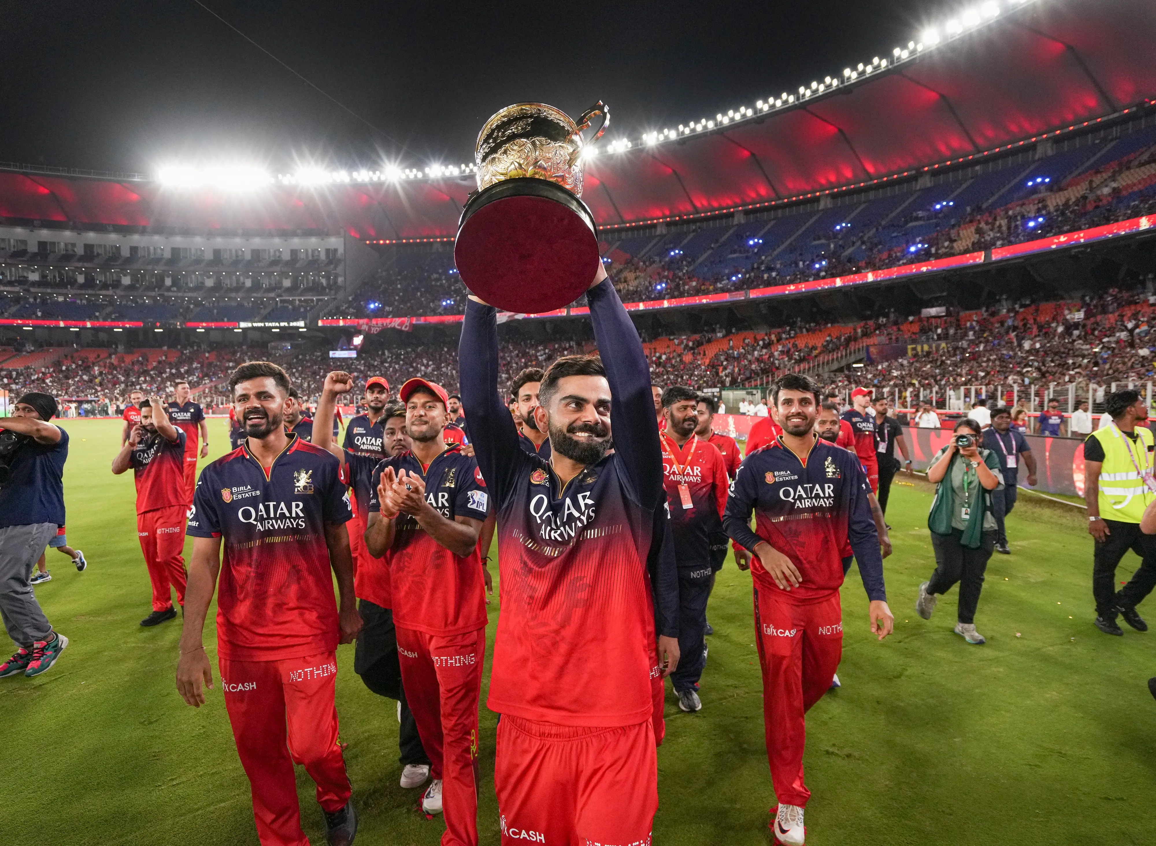 Royal Challengers Bengaluru's Virat Kohli, holding the trophy, walks on the ground after the team's win.