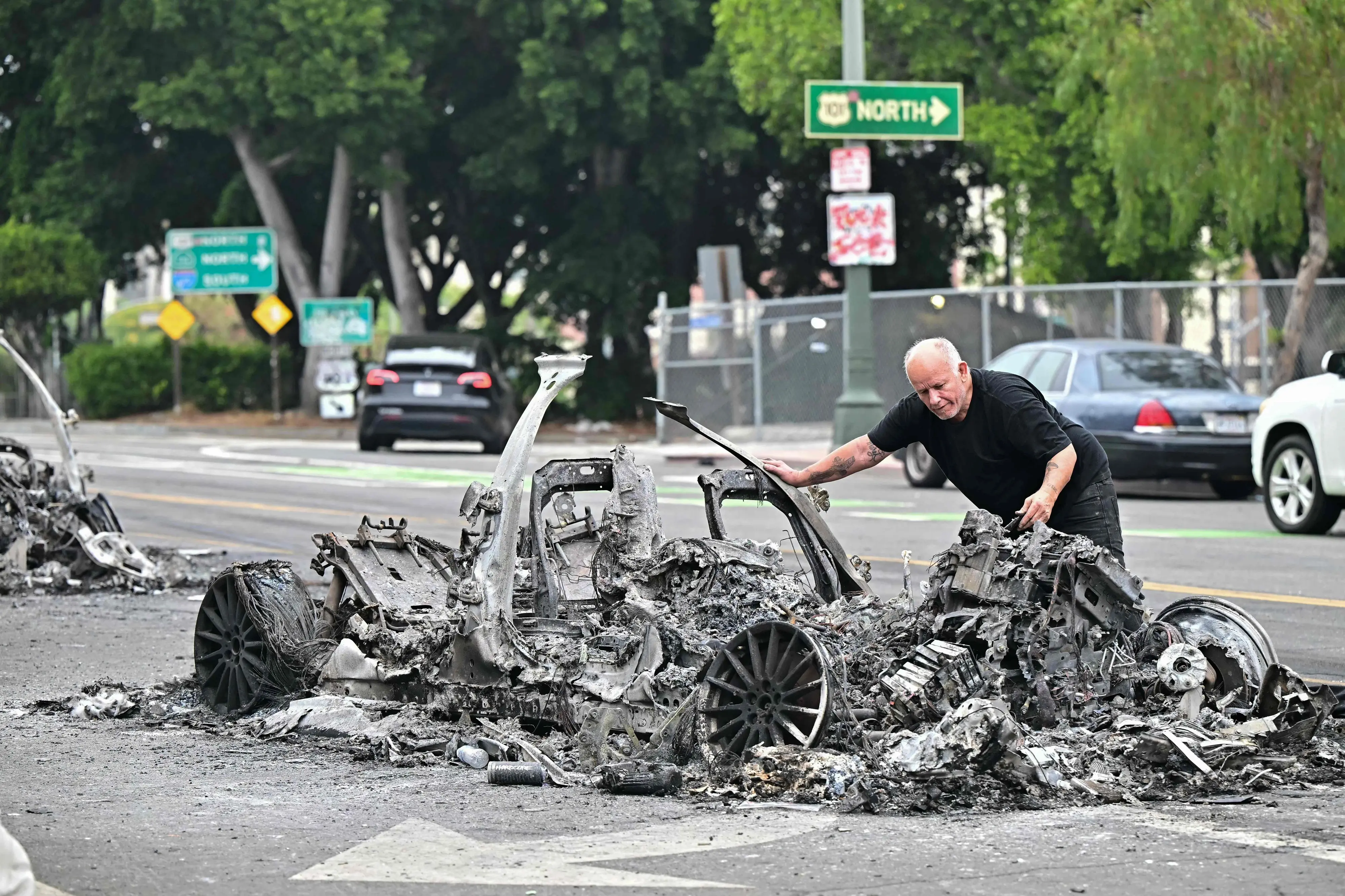 A man looks at the charred remains of a burned Waymo vehicle in the street following a night of protests in response to federal immigration operations in Los Angeles | AFP