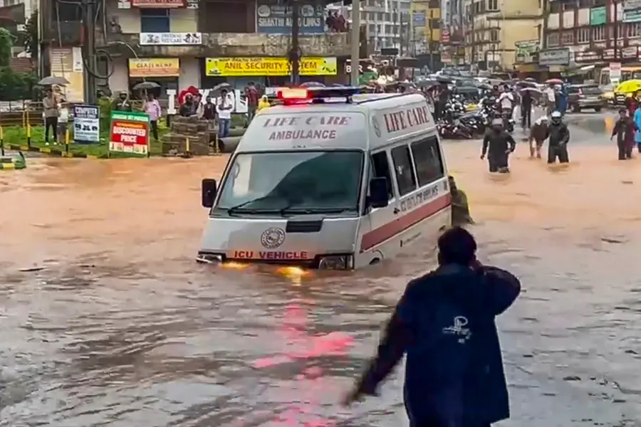 People push an ambulance while wading through a waterlogged road amid rainfall in Mangaluru