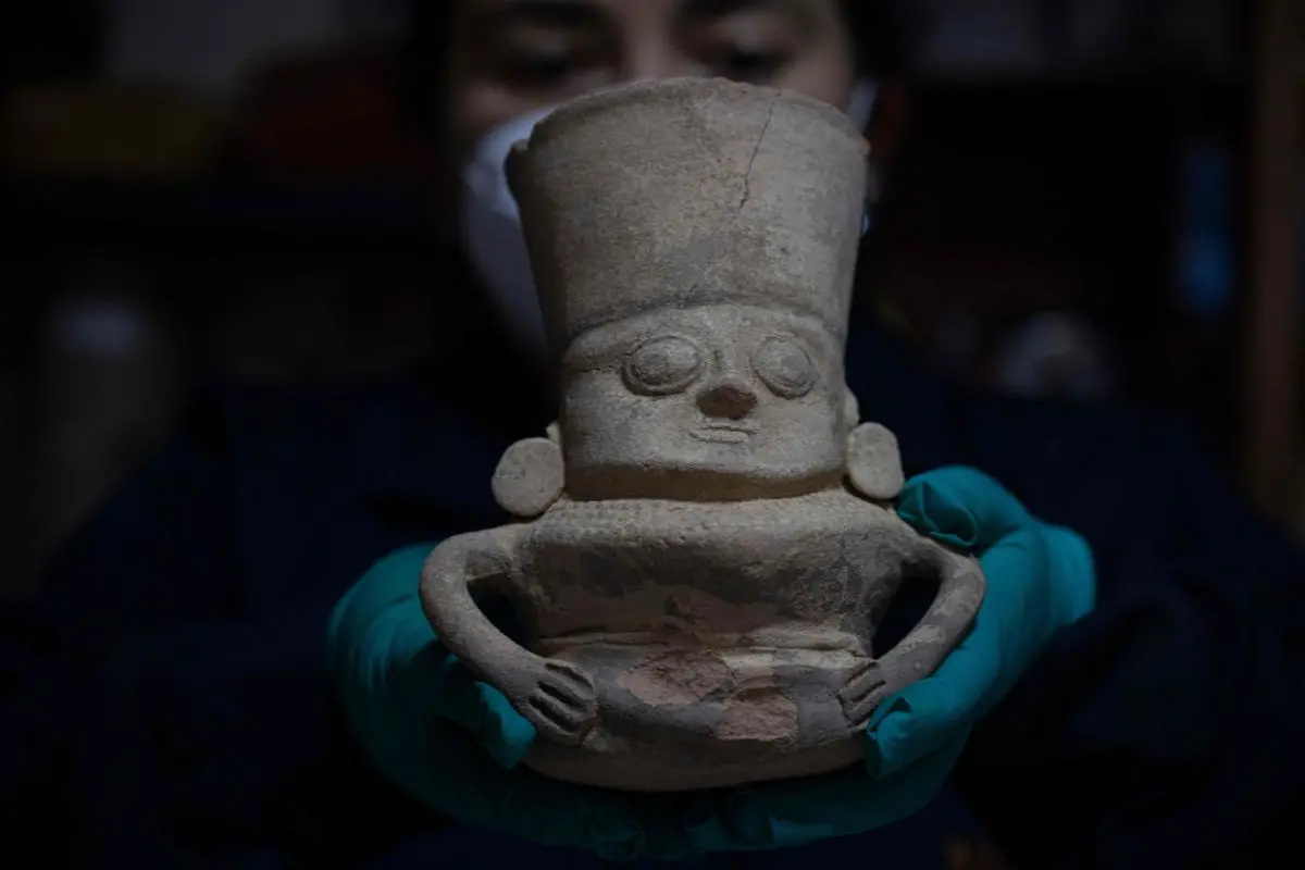An expert holds a piece while working around the remains of a pre-Hispanic burial that was found during an excavation to install a gas pipeline in Lima.