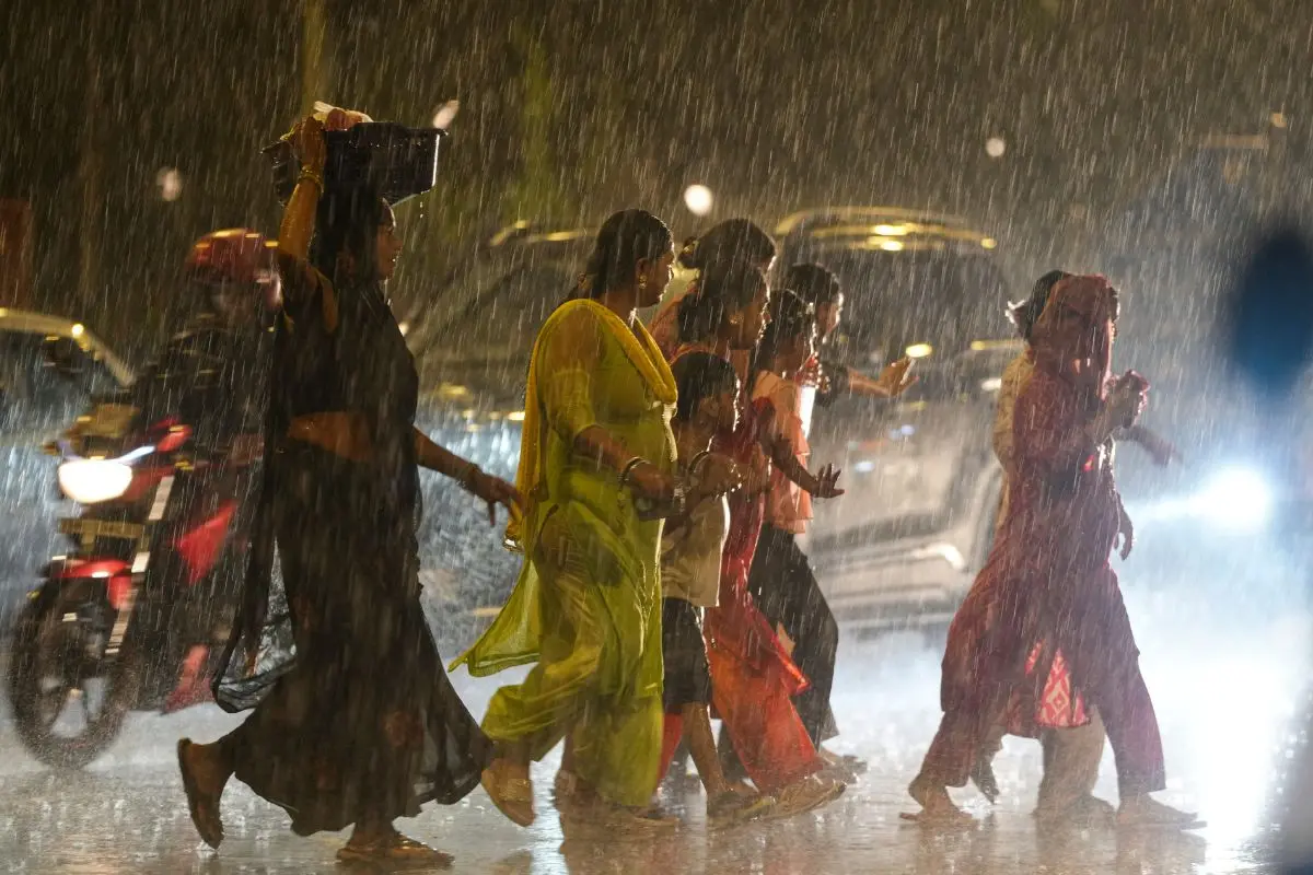 Commuters cross a road amid rainfall in New Delhi. Photo: PTI