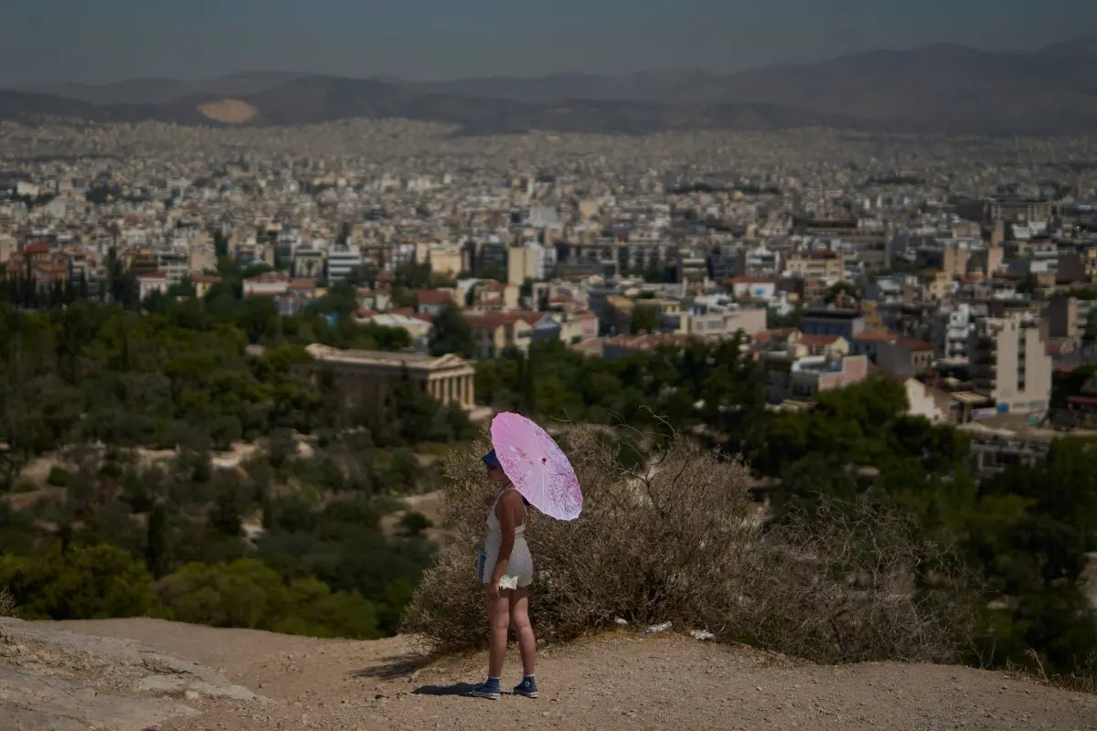 A tourist with an umbrella stands on Filopappou Hill as Athens stretches out in the background, Monday, July 7, 2025 (Photo: AP)