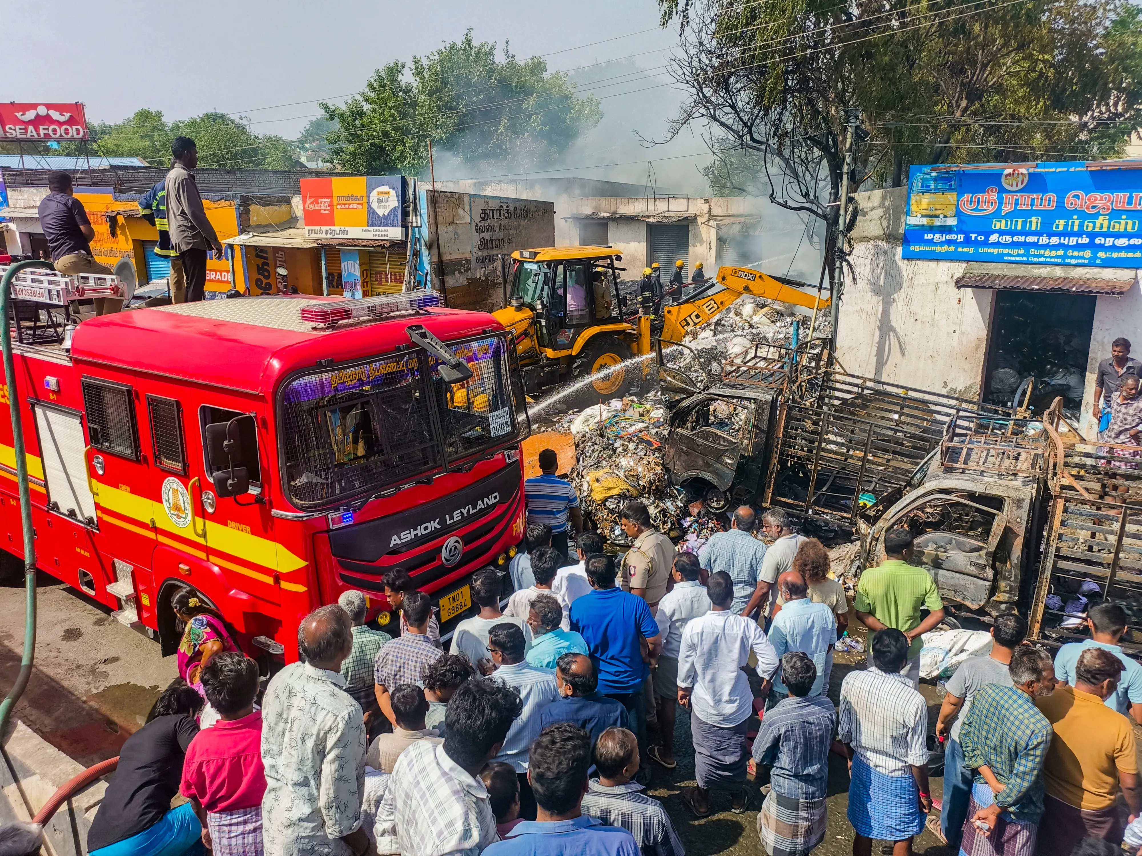 People gather as firefighters douse a fire which broke out at an old paper warehouse, in Madurai