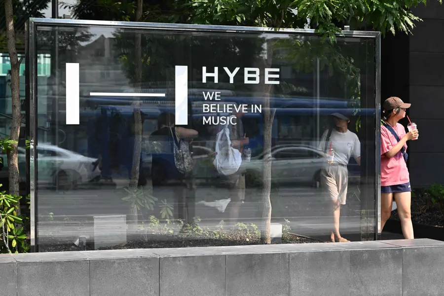 Pedestrians walk past the signage for HYBE
