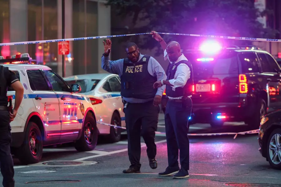 Police and others gather at a crime scene in midtown Manhattan after two people, including a police officer, were shot inside of an office building