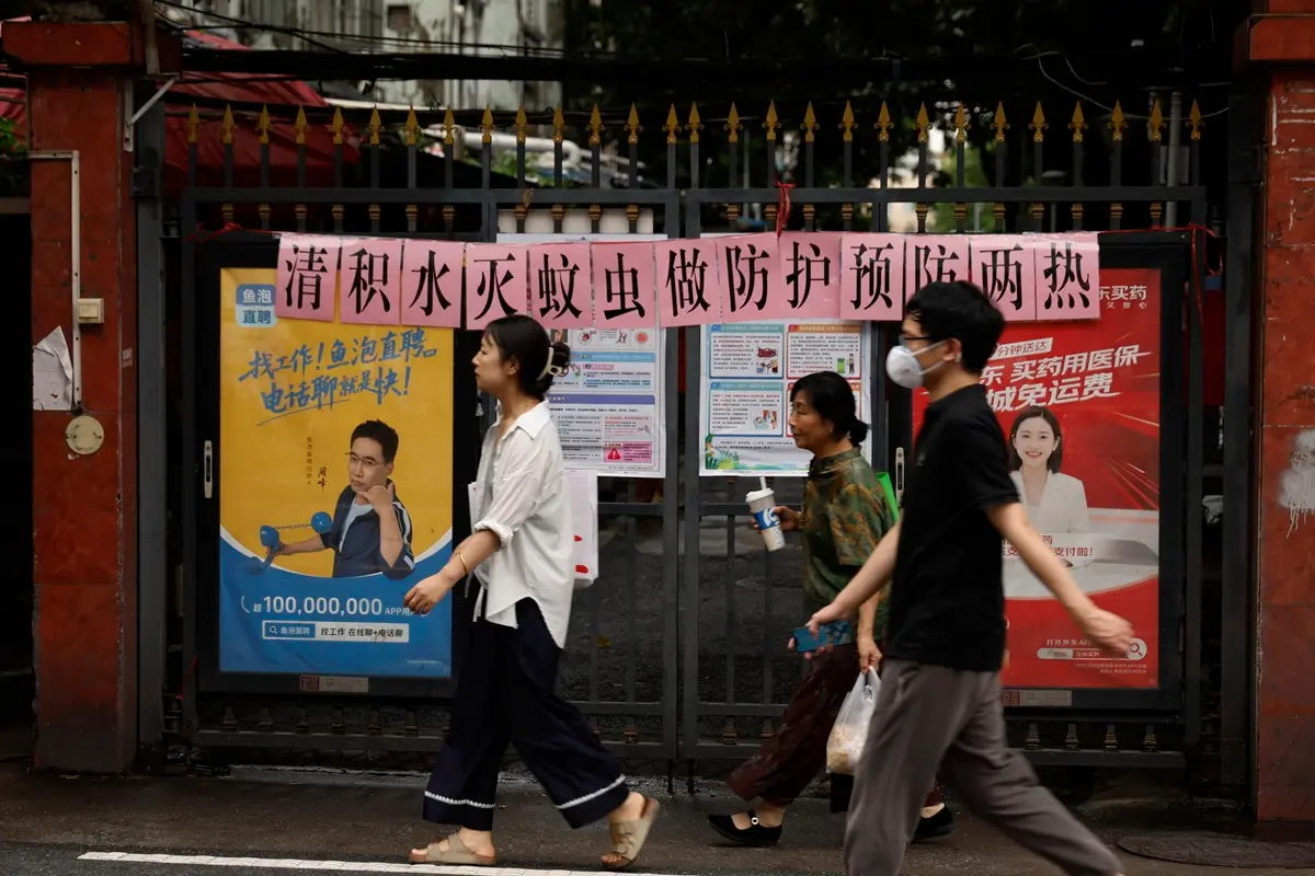 Residents walk past a residential entrance gate displaying a slogan urging mosquito control, in Guangzhou, south China's Guangdong Province | Photo: AP