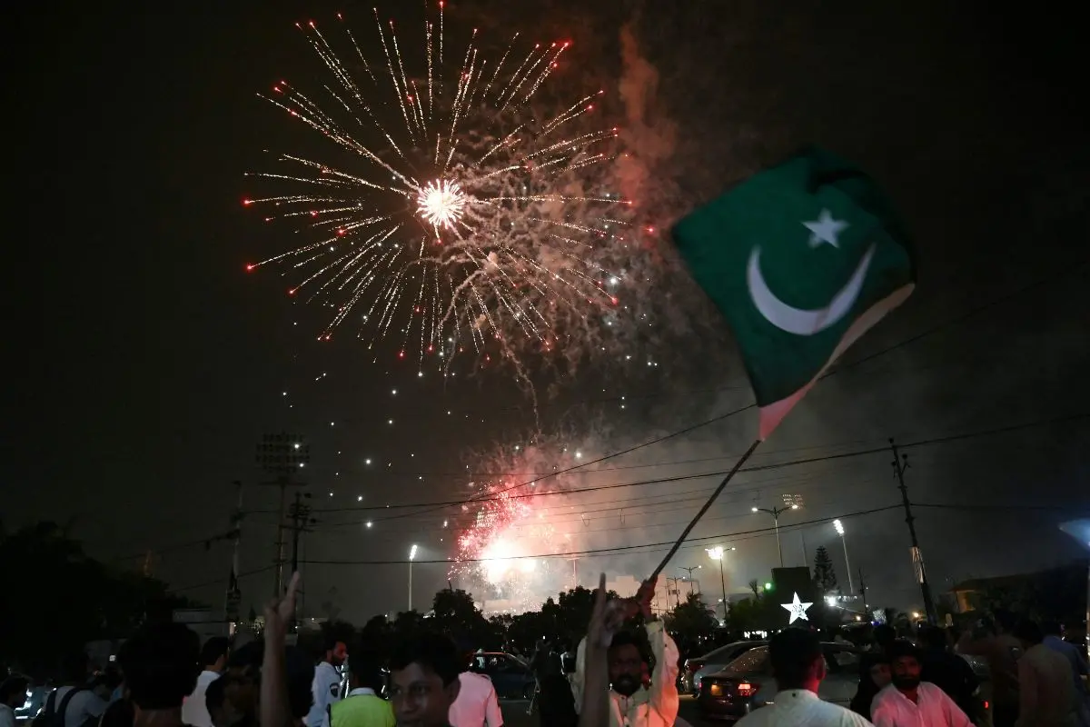 A man waves a flag of Pakistan as people watch a firework displayed in front of the National Stadium during Pakistan's 78th anniversary of Independence Day celebrations in Karachi on August 14(Photo: AFP)