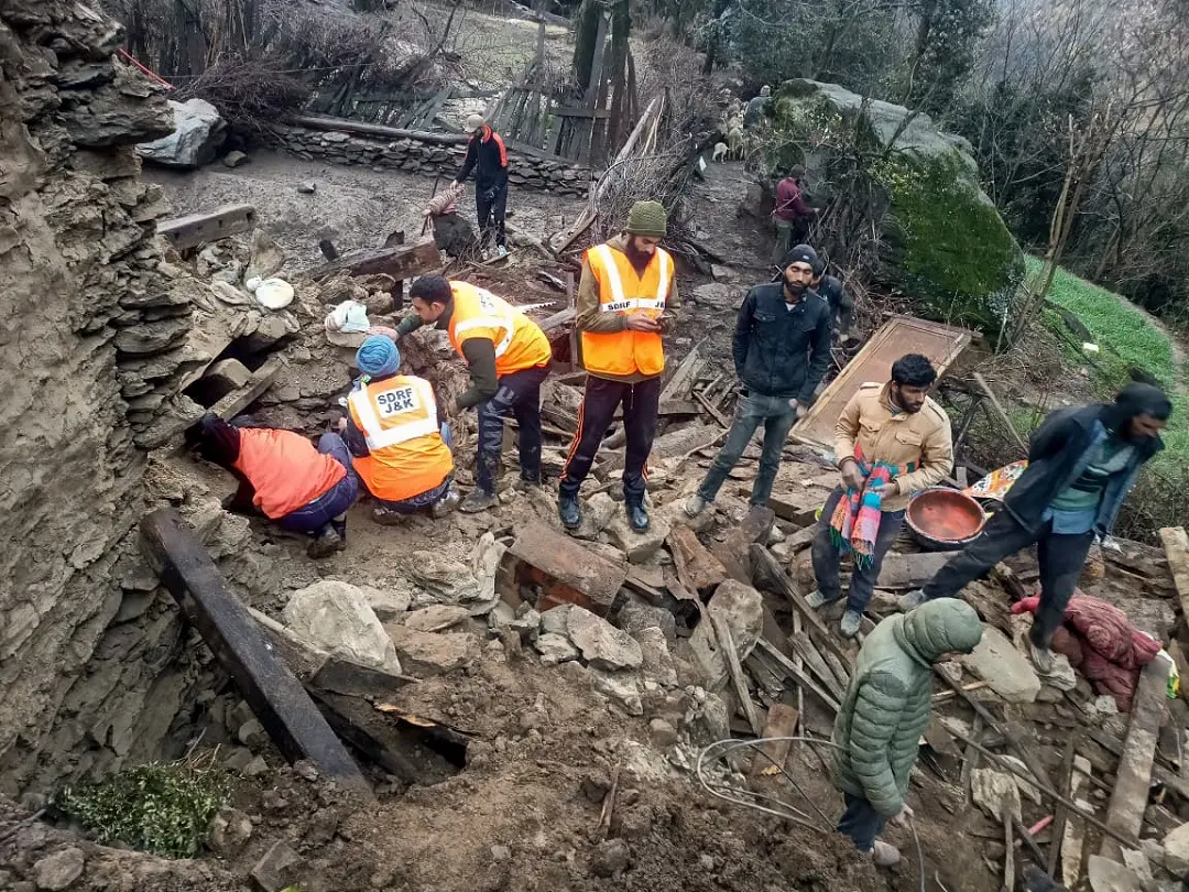Jammu and Kashmir State Disaster Response Force (SDRF) personnel and people gather near the remains of the residential houses that were partially damaged in Kishtwar | ANI