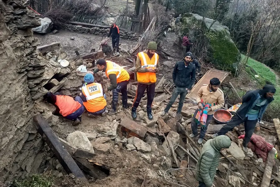 Jammu and Kashmir State Disaster Response Force (SDRF) personnel and people gather near the remains of the residential houses that were partially damaged\u00A0in Kishtwar