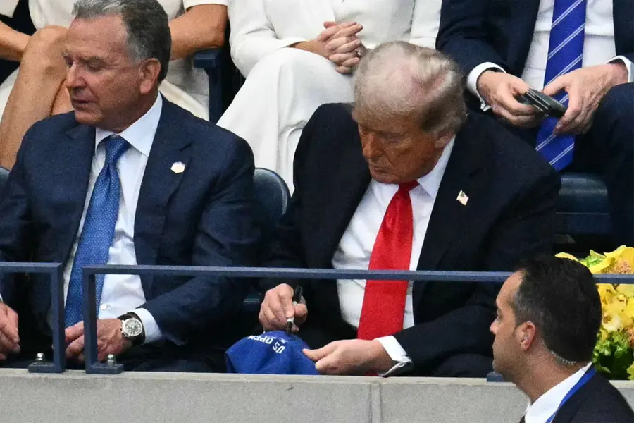 US President Donald Trump (R) signs a hat as he attends the men's singles final tennis match between Spain’s Carlos Alcaraz and Italy’s Jannik Sinner