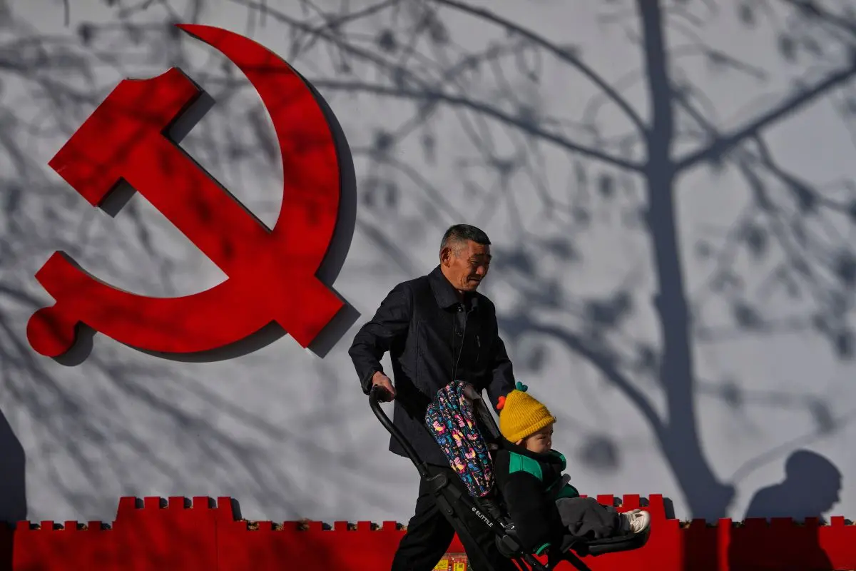 A man walks with a toddler past by a Communist Party's logo on display near a residential area in Beijing (File photo: AP)